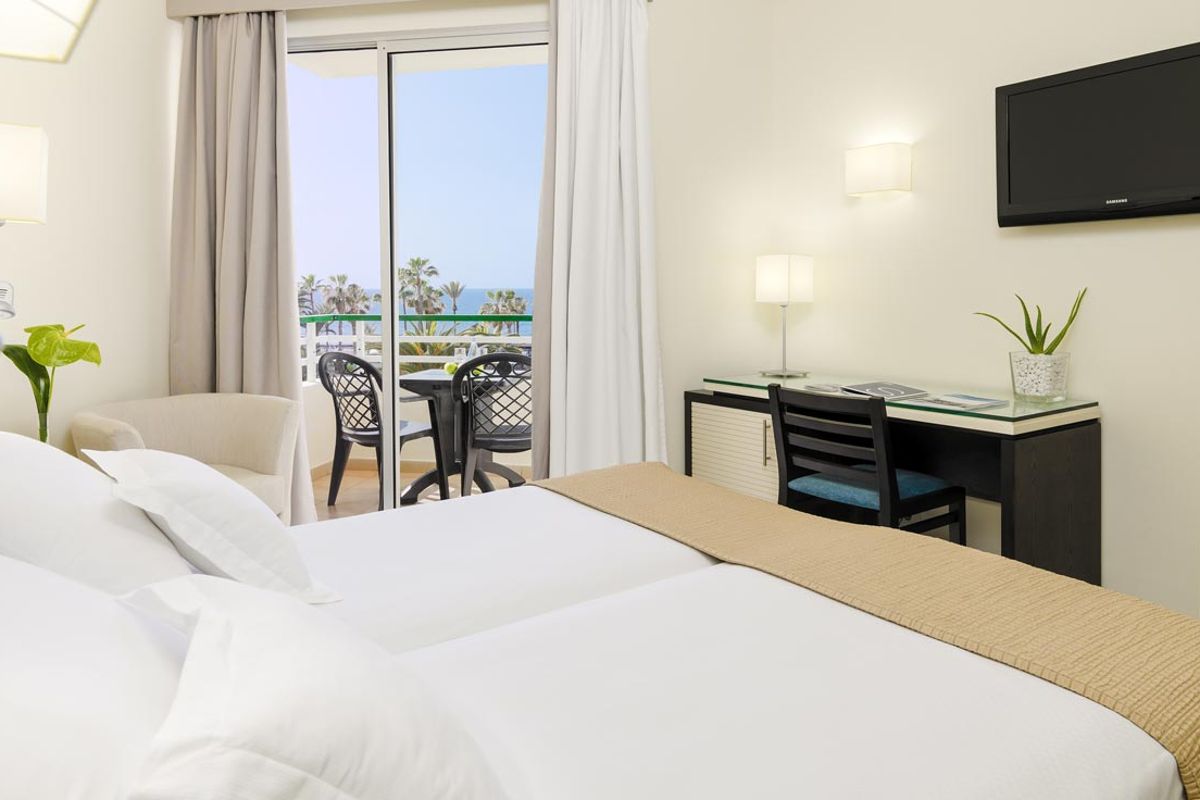 Hotelkamer op Tenerife met bed, bureau, balkon en zeezicht.