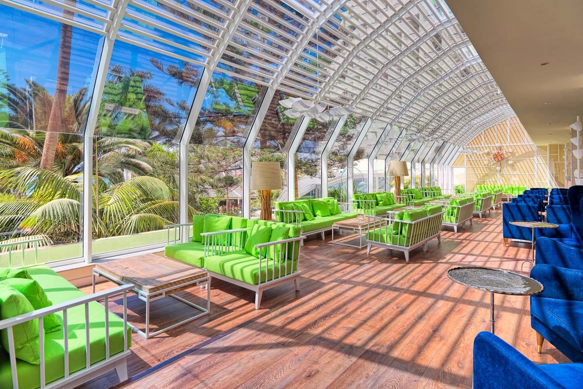 Een lichte woonkamer met groene en blauwe banken op Tenerife met palmbomen buiten.