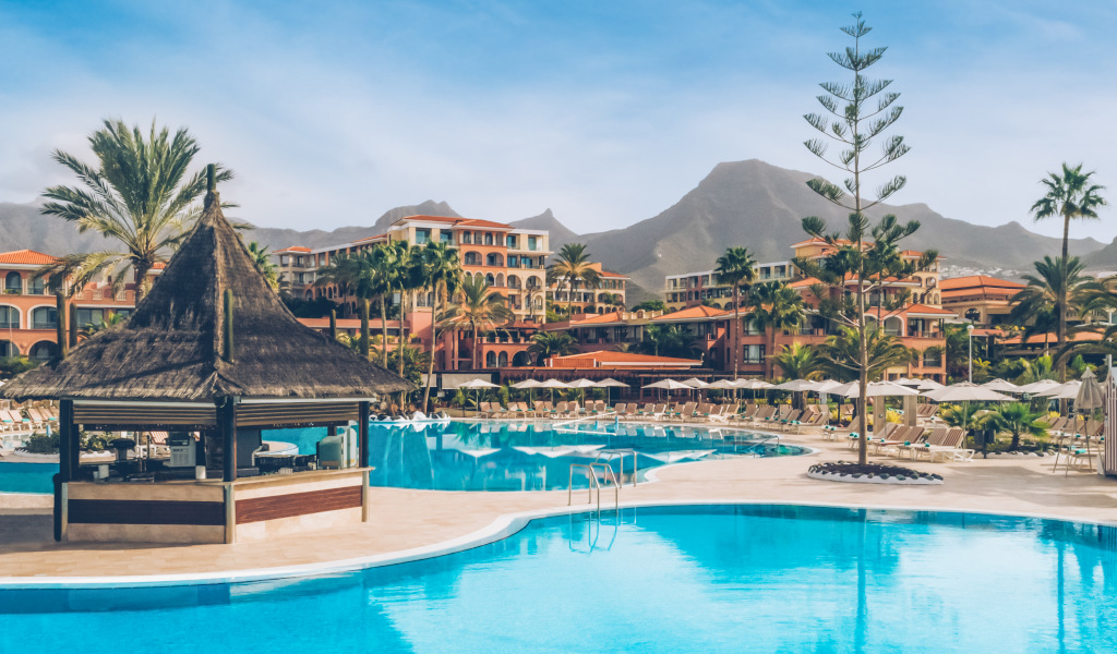 Hotelzwembad op Tenerife met bergen op de achtergrond en parasols.