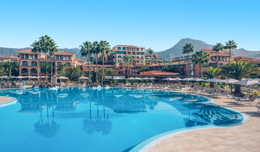 Het zwembad van een hotel omringd door palmbomen en bergen op Tenerife.