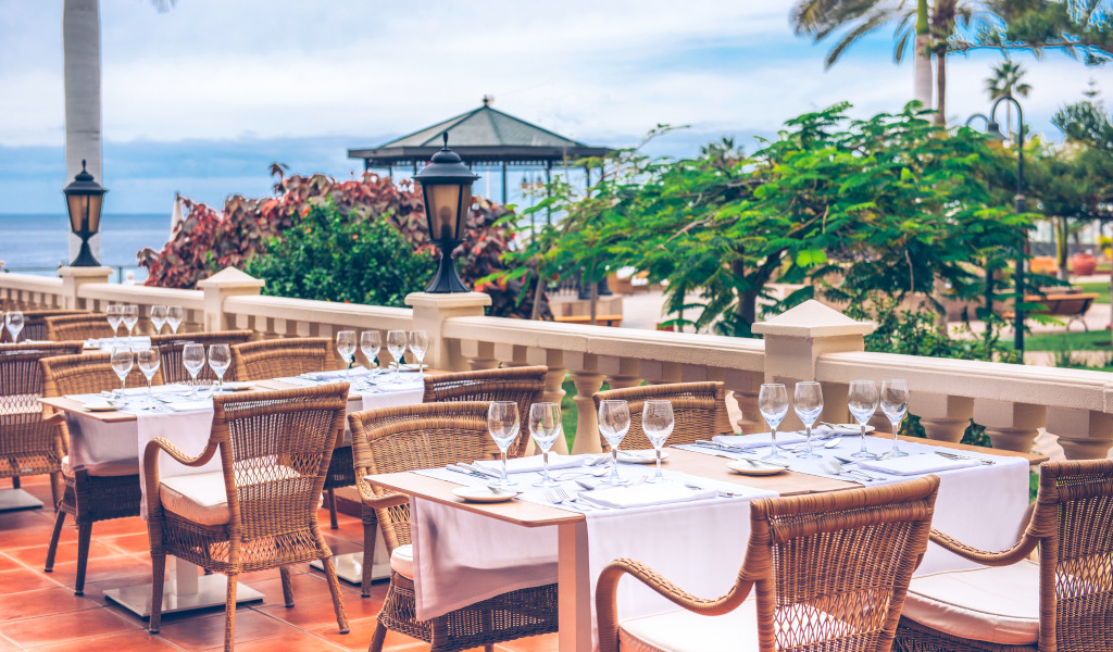 Terras met tafels en stoelen in een restaurant op Tenerife, zeezicht op de achtergrond.