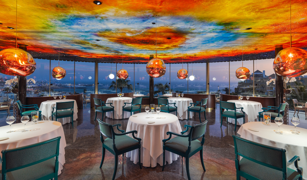 Restaurant met zeezicht bij schemering op Tenerife, hanglampen en kleurrijk plafond.
