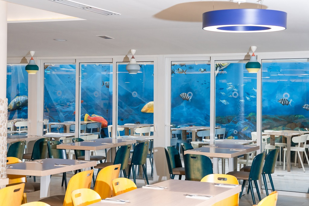 Eetzaal met een oceaanmuurschildering en kleurrijke stoelen in een restaurant op Tenerife.