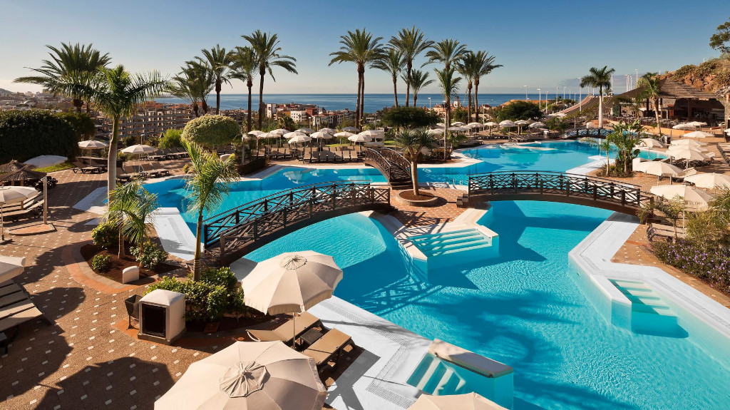Buitenzwembad omringd door palmbomen en ligstoelen in een hotel op Tenerife.