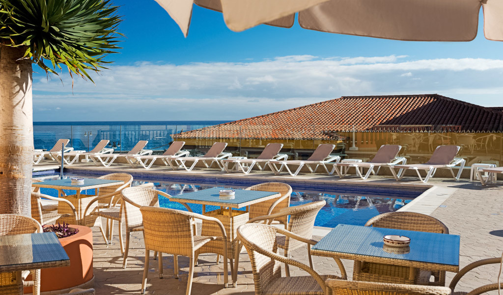 Terras met tafels en stoelen bij het zwembad en ligstoelen, zeezicht op Tenerife.