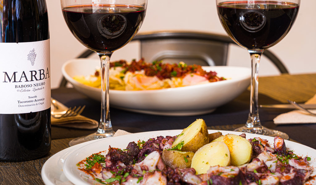 Octopusgerecht met aardappelen, een fles Marba Baboso Negro en twee glazen rode wijn in Tacoronte-Acentejo.