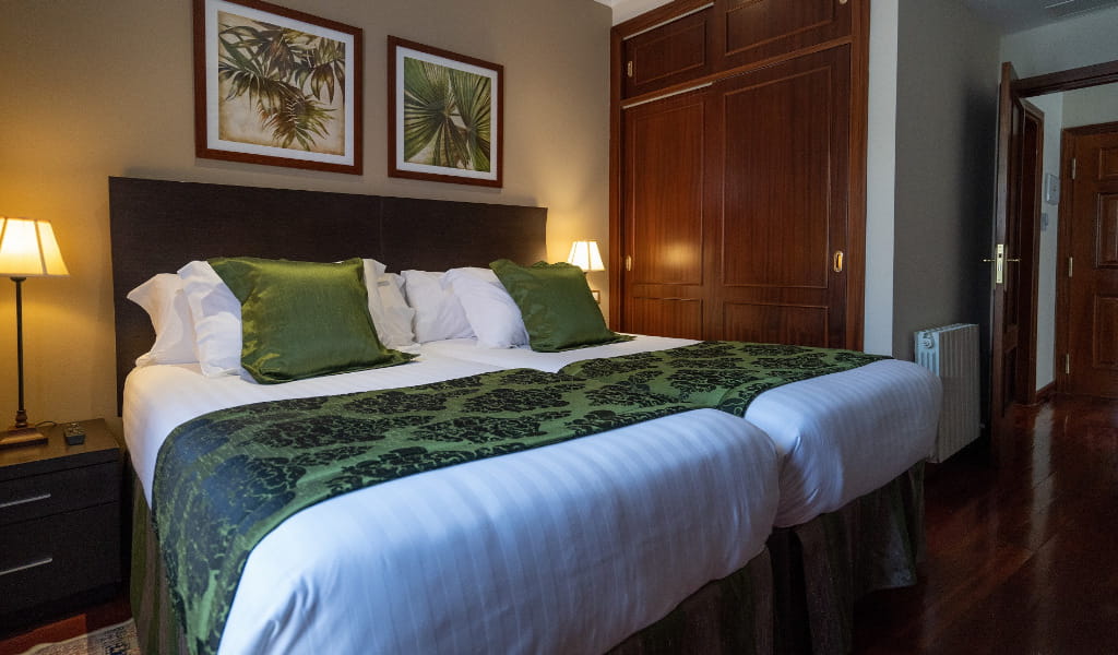 Kamer met twee eenpersoonsbedden, verbonden met een donker hoofdeinde en groene kussens.