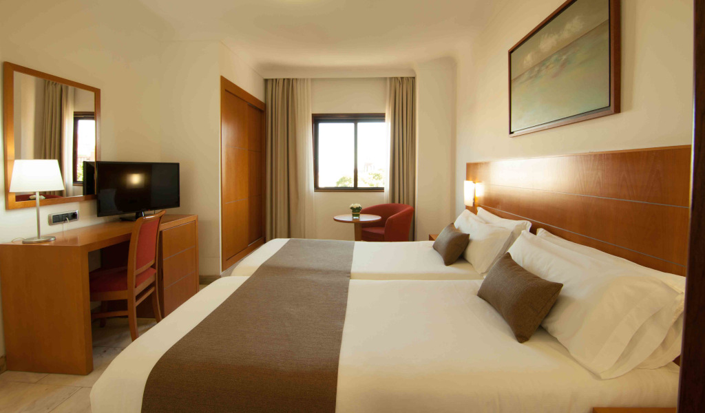 Hotelkamer met twee bedden, bureau met tv en raam.