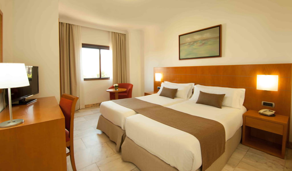 Tweepersoonskamer met eenpersoonsbedden, bureau, tv en raam op Tenerife.