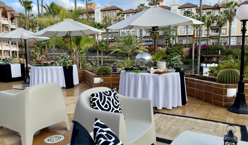 Terras op Tenerife met tafels en parasols, omgeven door groen en gebouwen.