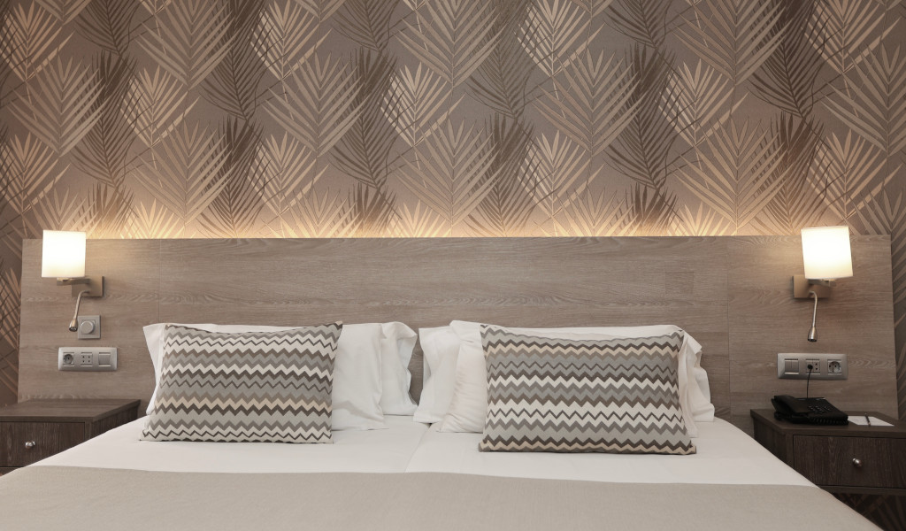 Dubbelbed met houten hoofdeinde en wandlampen in hotelkamer op Tenerife.
