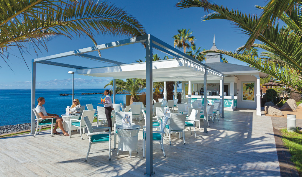 Terras met tafels en stoelen aan zee op Tenerife, de serveerster brengt drankjes.
