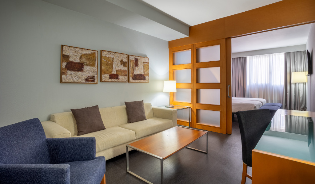 Hotelwoonkamer op Tenerife met bank, tafel, lamp en schuifdeur.