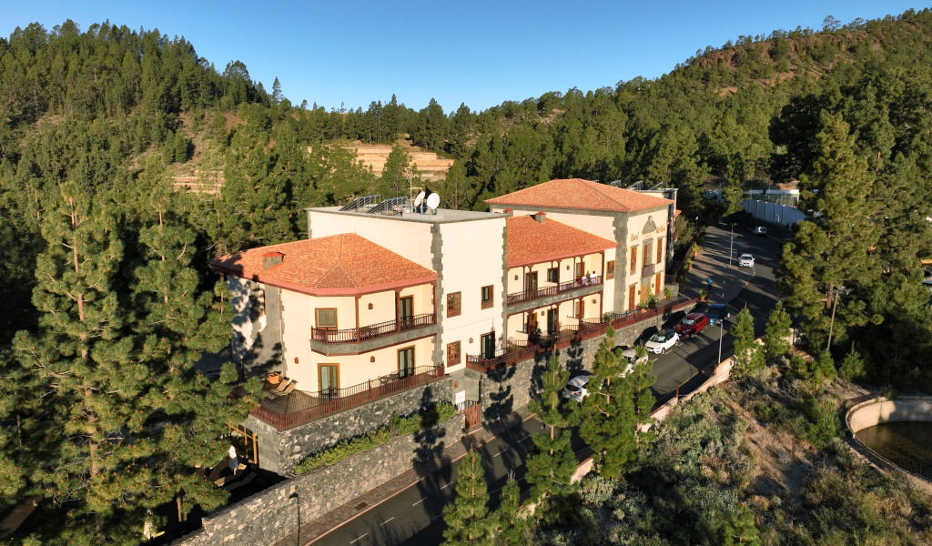 Gebouw omringd door dennen in Vilaflor, Tenerife, met auto's ervoor geparkeerd.