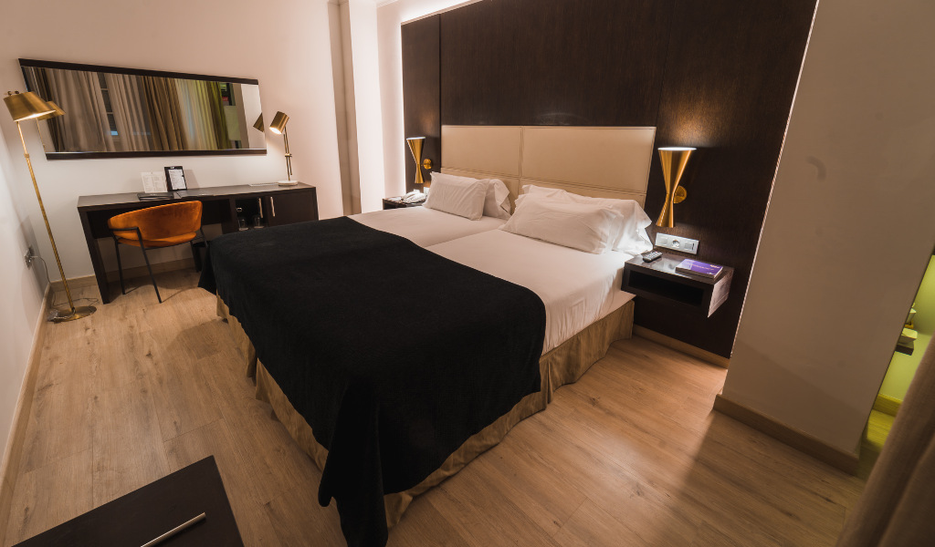 Tweepersoonsbed in hotelkamer in Santa Cruz de Tenerife met bureau en elegante spiegel.