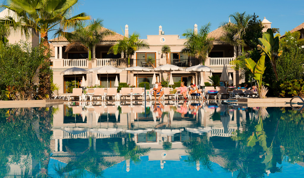 Zwembad met ligstoelen en parasols voor een hotel omringd door palmbomen op Tenerife.