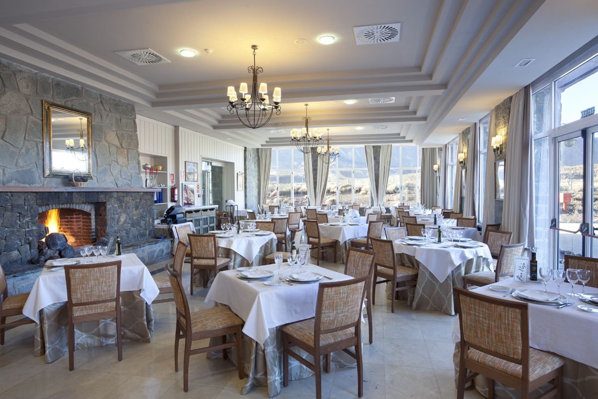 Restaurant met panoramisch raam en open haard op Tenerife, tafels bedekt met witte tafelkleden.