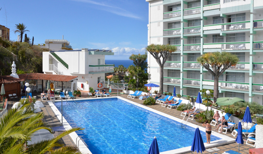 Hotelzwembad op Tenerife met ligstoelen en uitzicht op de oceaan.