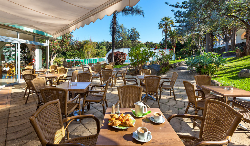 Terras met tafels en stoelen in een tuin op Tenerife, croissants en koffie op tafel.