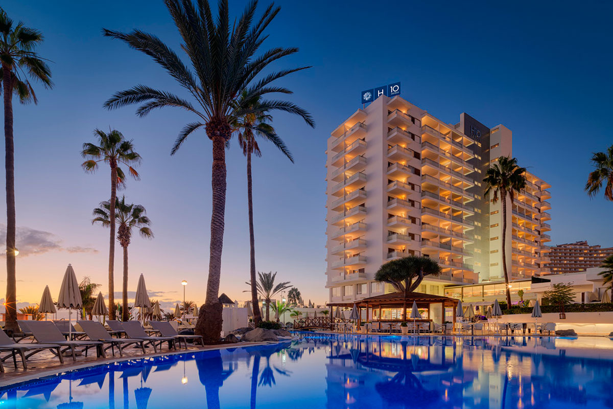Hotel met zwembad bij zonsondergang op Tenerife, omringd door palmbomen en ligstoelen.