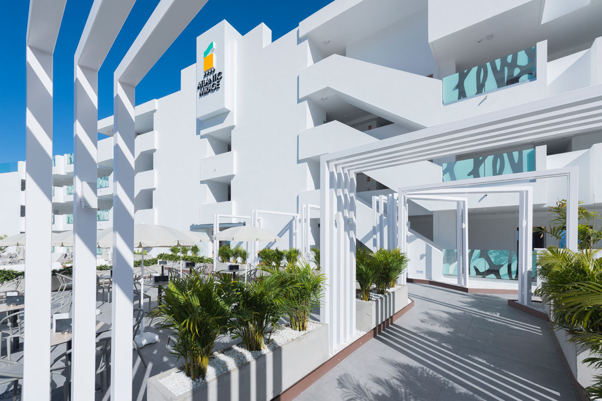 Moderne ingang van het Atlantic Mirage hotel op Tenerife, met planten en paraplu's.