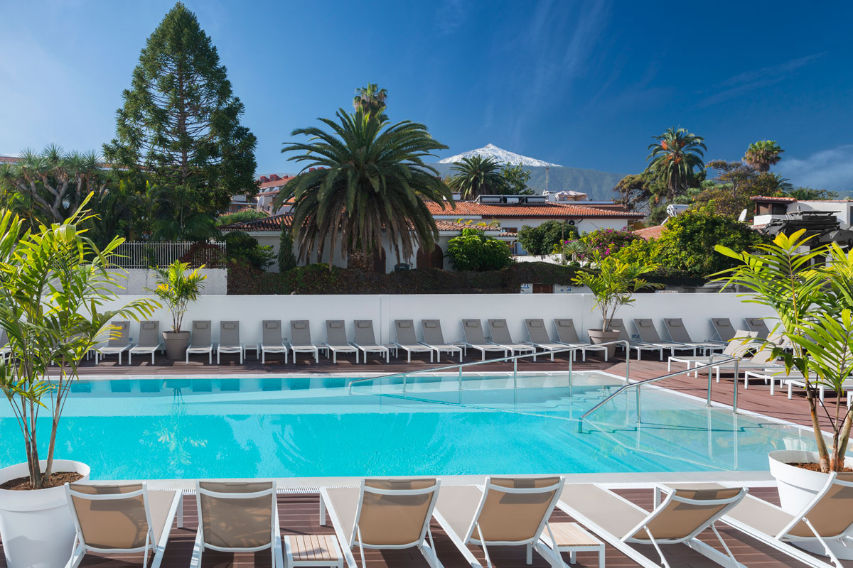 Buitenzwembad op Tenerife met stoelen en palmbomen overal.