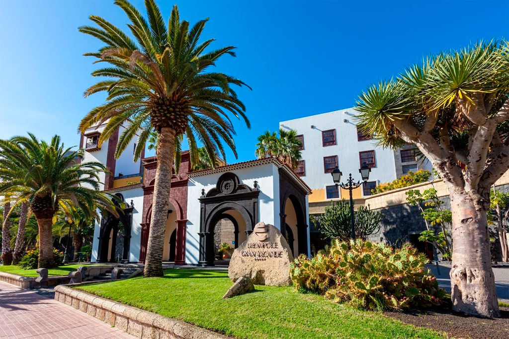Gebouw met palmbomen en cactussen in Garachico, Tenerife. Rocktekst: Convento San Francisco.