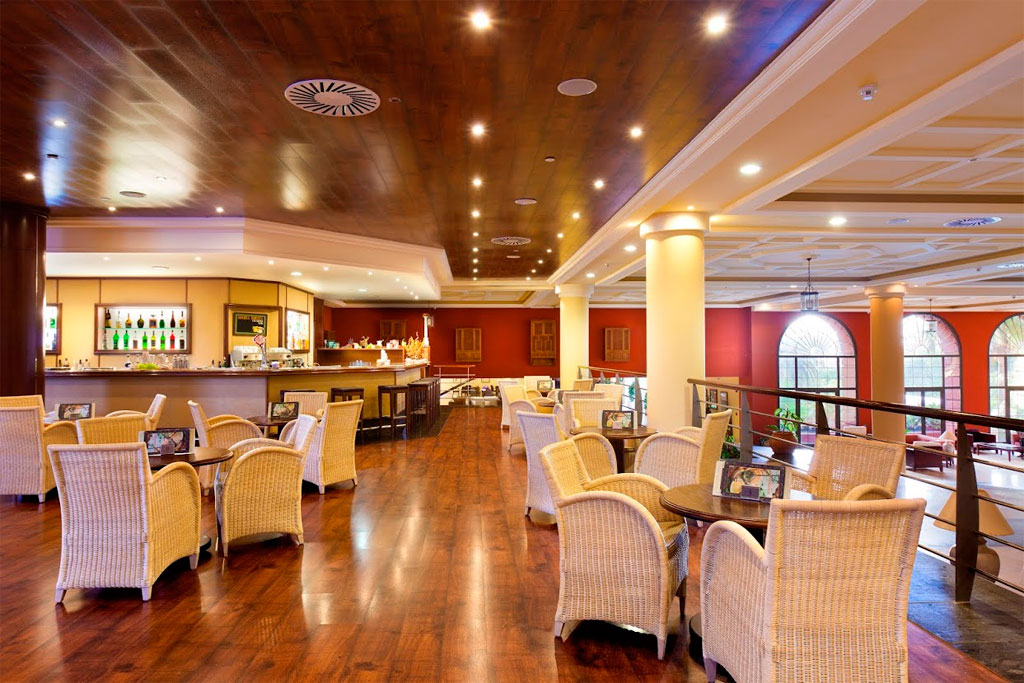 Lounge van een hotel op Tenerife met tafels, rotanen stoelen en een verlichte bar.