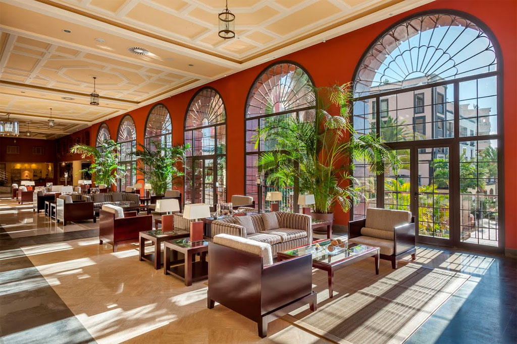 Woonkamer met banken, tafels en grote boogvormige ramen in een hotel op Tenerife.