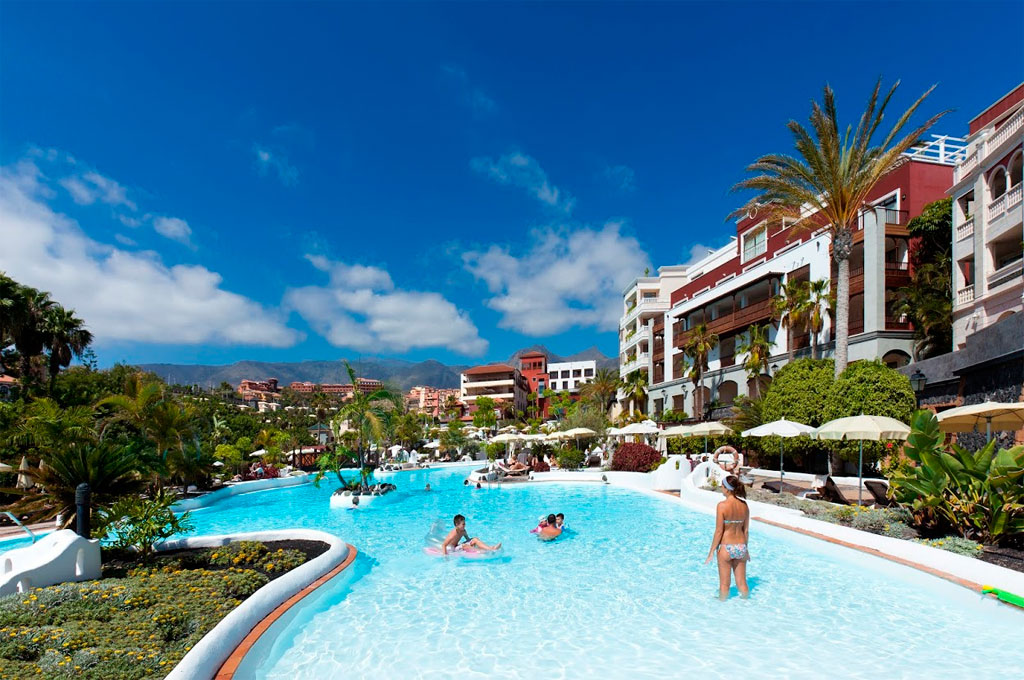 Zwembad omringd door palmbomen en gebouwen in een hotel op Tenerife.