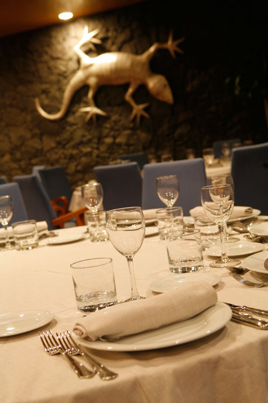 Restauranttafel op Tenerife met elegant bestek en glazen. Hagedisstandbeeld aan de muur.