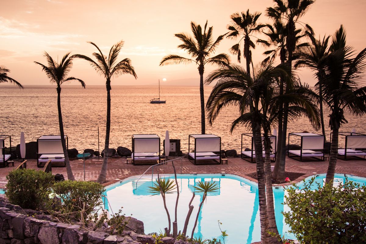 Zwembad met palmbomen bij zonsondergang aan zee op Tenerife.