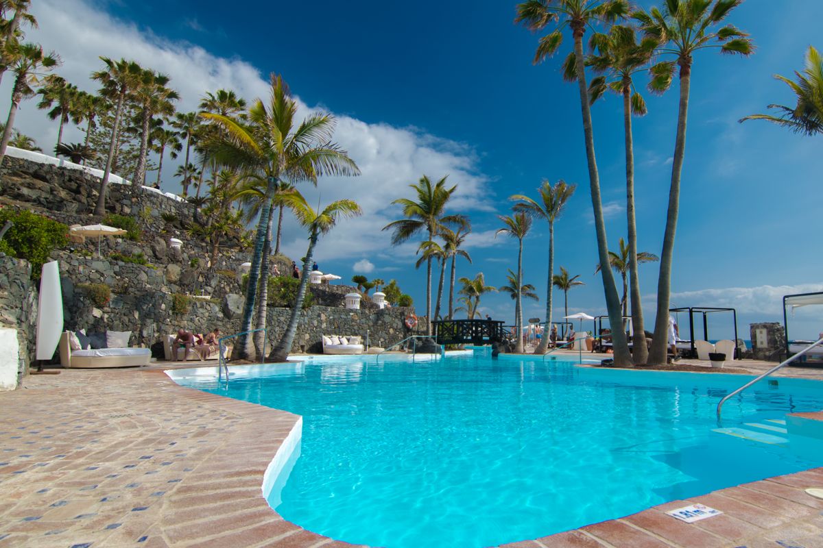 Zwembad met palmbomen en ligstoelen in een resort op Tenerife.