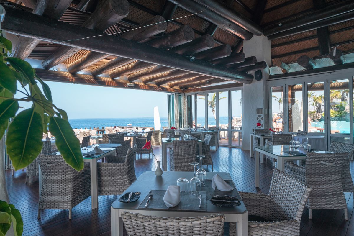 Restaurant met zeezicht op Tenerife, rotaan meubels en een houten balkenplafond.
