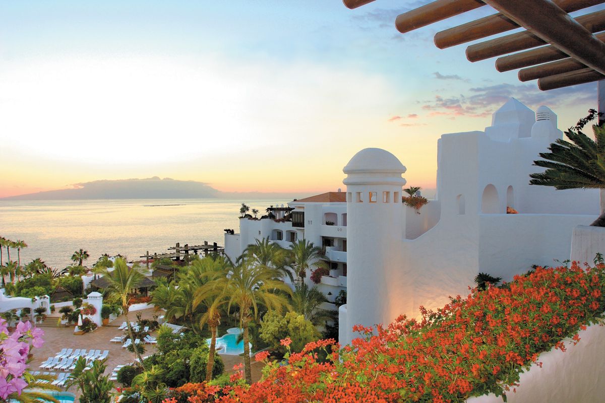 Uitzicht op een hotel aan het strand bij zonsondergang op Tenerife, omringd door palmbomen.