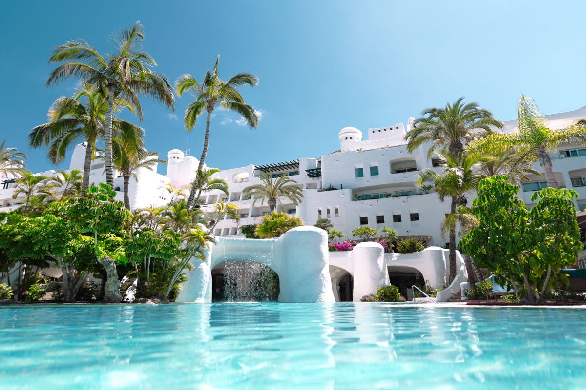 Wit hotel met zwembad en palmbomen op Tenerife, heldere lucht.