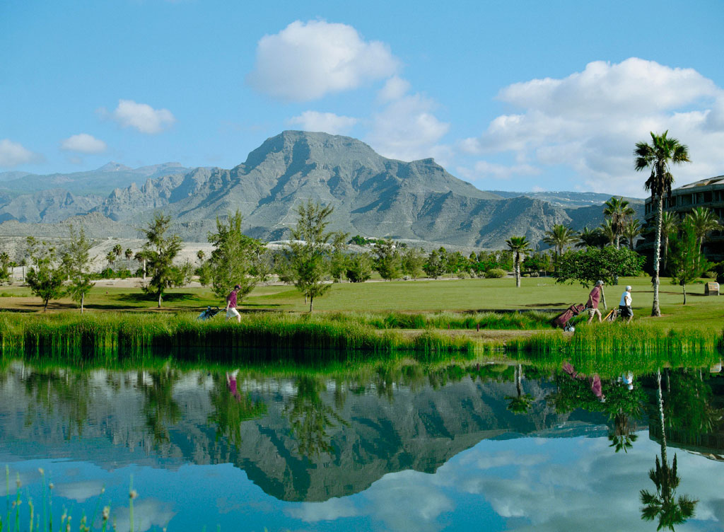 Golfbaan op Tenerife met bergen op de achtergrond en reflectie in het meer.