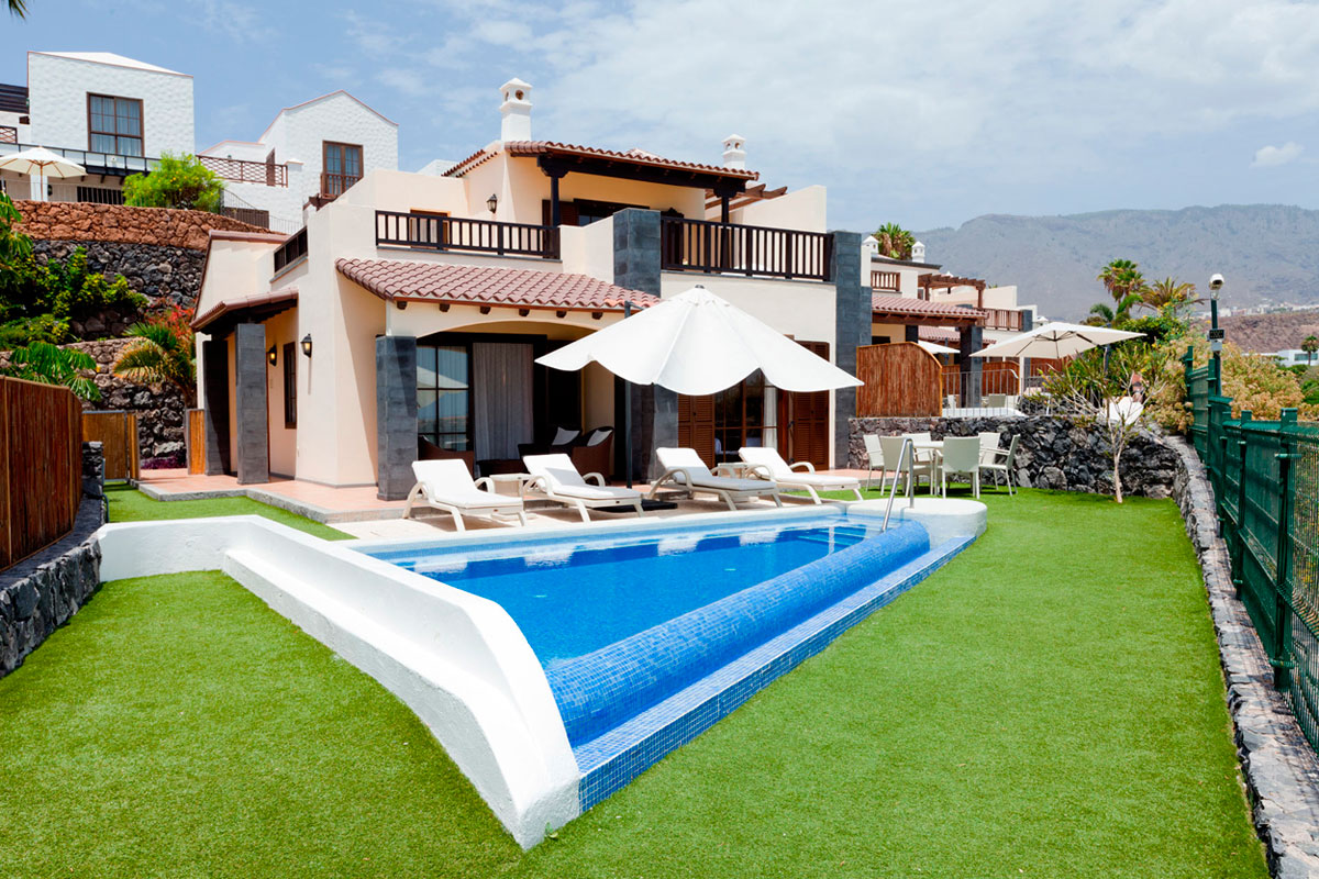 Huis met zwembad en strandstoelen op Tenerife, omringd door gras en bergen op de achtergrond.
