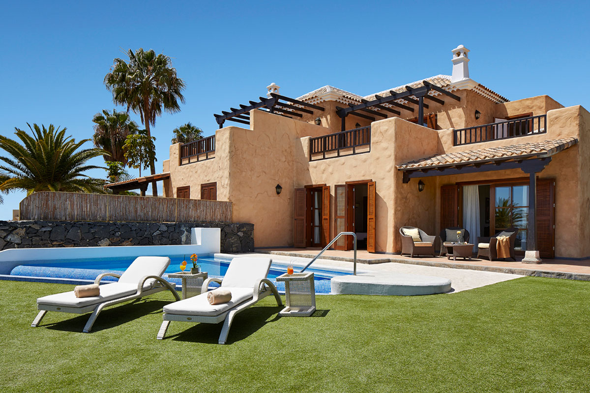 Villa met zwembad op Tenerife, gazon en ligstoelen ervoor, omringd door palmbomen.