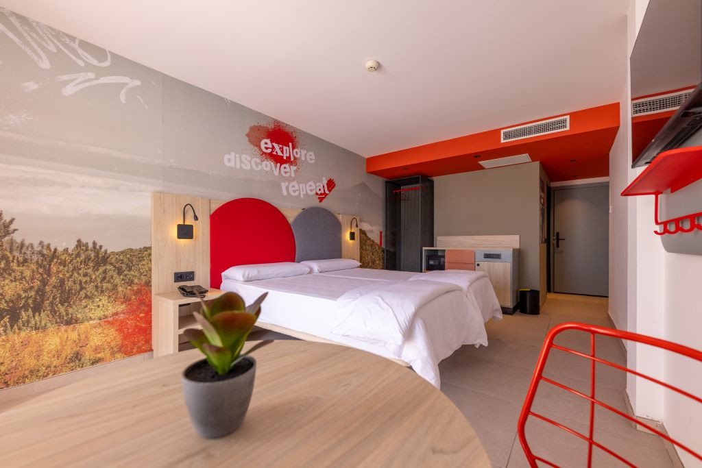 Moderne kamer met tweepersoonsbed, plattegrond en muurschildering die zegt explore, ontdek herhaling.