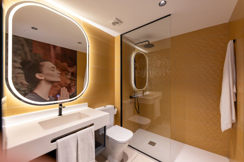 Badkamer met douche, wastafel, verlichte spiegel en foto van een vrouw die mediteert op Tenerife.