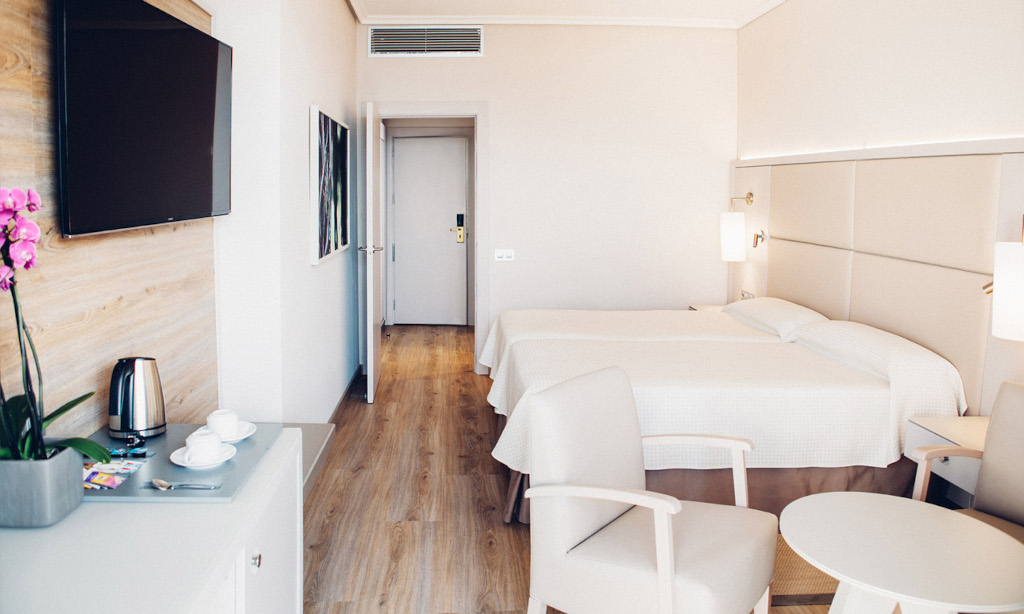 Hotelkamer op Tenerife met eenpersoonsbedden, tafel, stoelen en tv aan de muur.