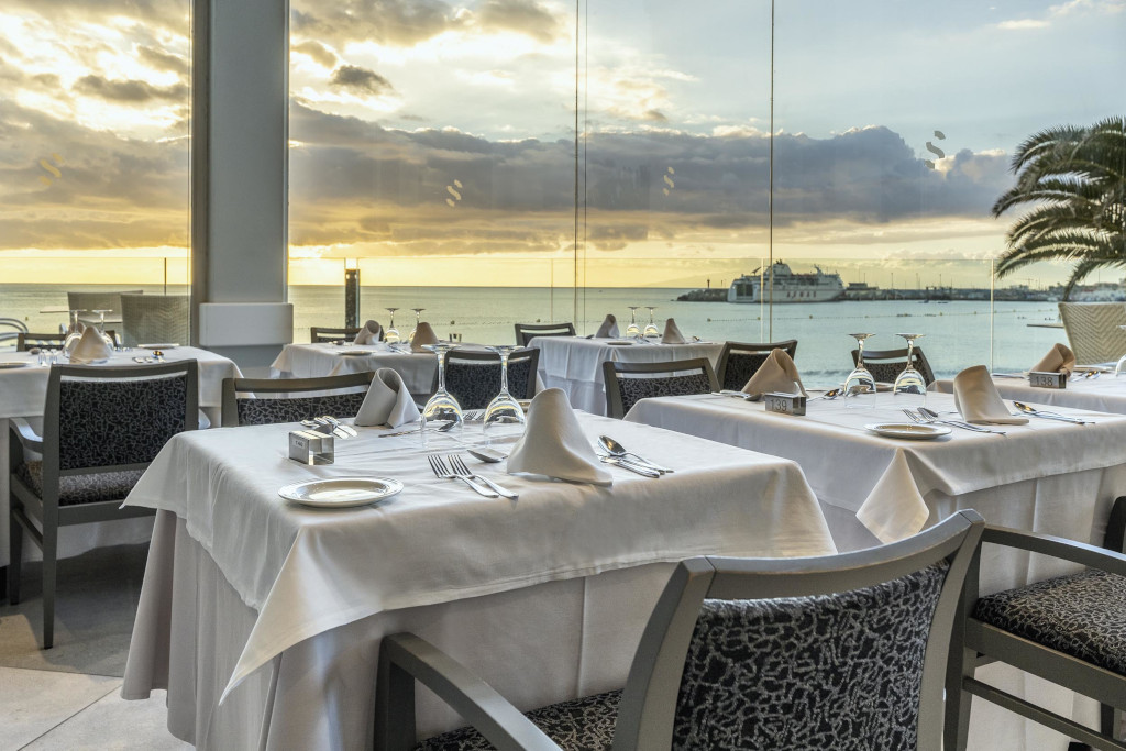 Tafels gedekt in een restaurant met uitzicht op zee en de haven op Tenerife bij zonsondergang.