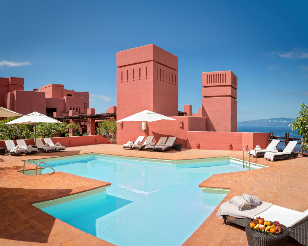 Zwembad omringd door ligstoelen en terracotta rode gebouwen met uitzicht op zee op Tenerife.