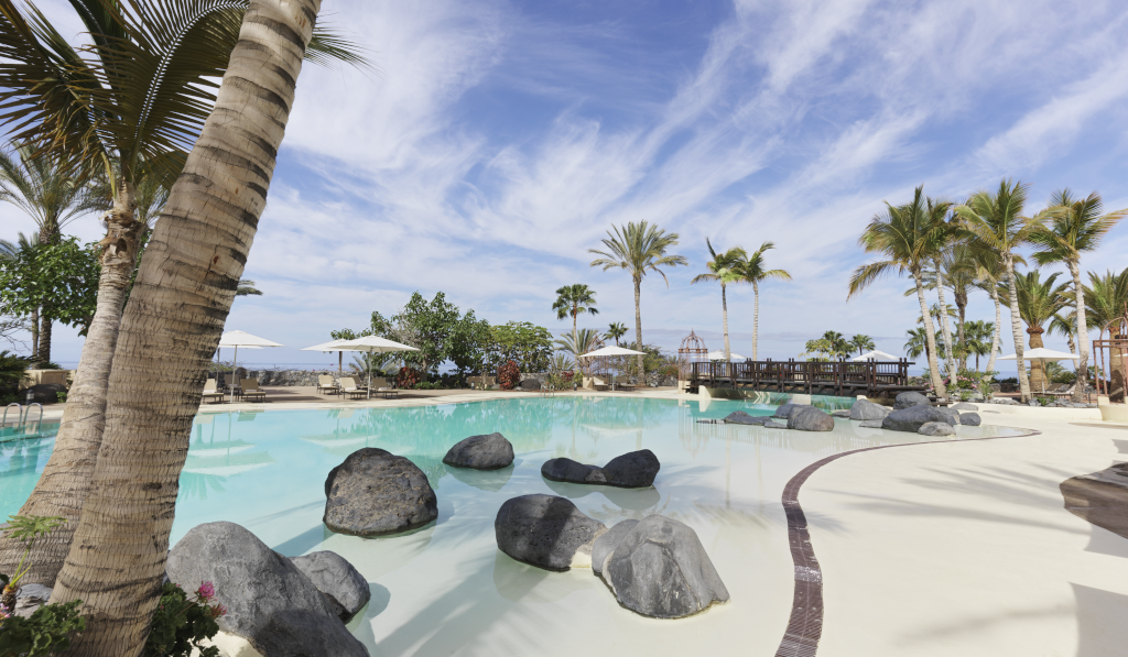 Zwembad met palmbomen en rotsen in een resort op Tenerife.