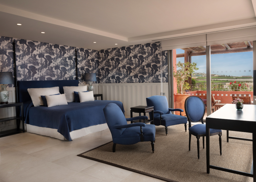 Hotelkamer op Tenerife met bed, blauwe fauteuils en een terras met uitzicht naar buiten.