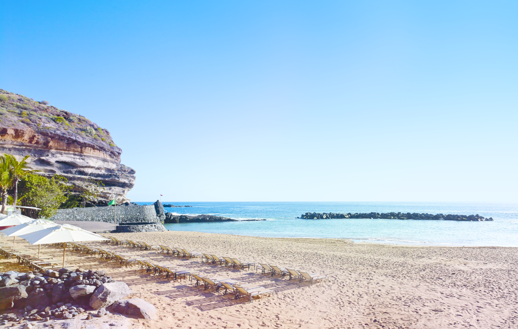 Strand met parasols en ligstoelen op Tenerife. Zee en klif aan de linkerkant.