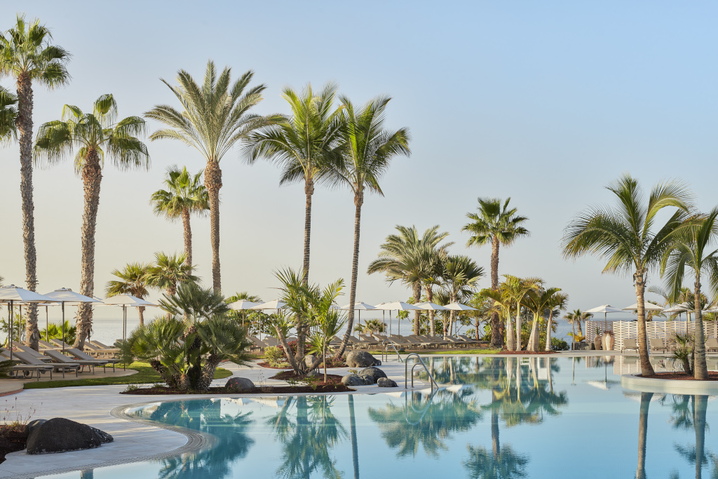 Zwembad omringd door palmbomen in een hotel op Tenerife met heldere luchten.