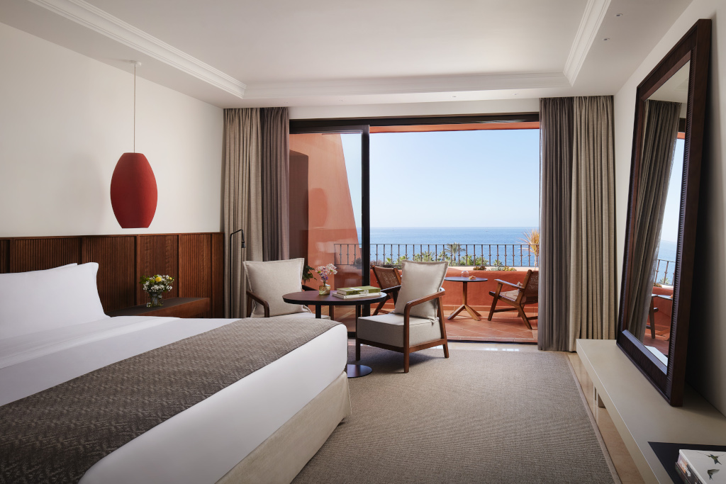 Hotelkamer met zeezicht op Tenerife, groot bed en balkon met tafels en stoelen.