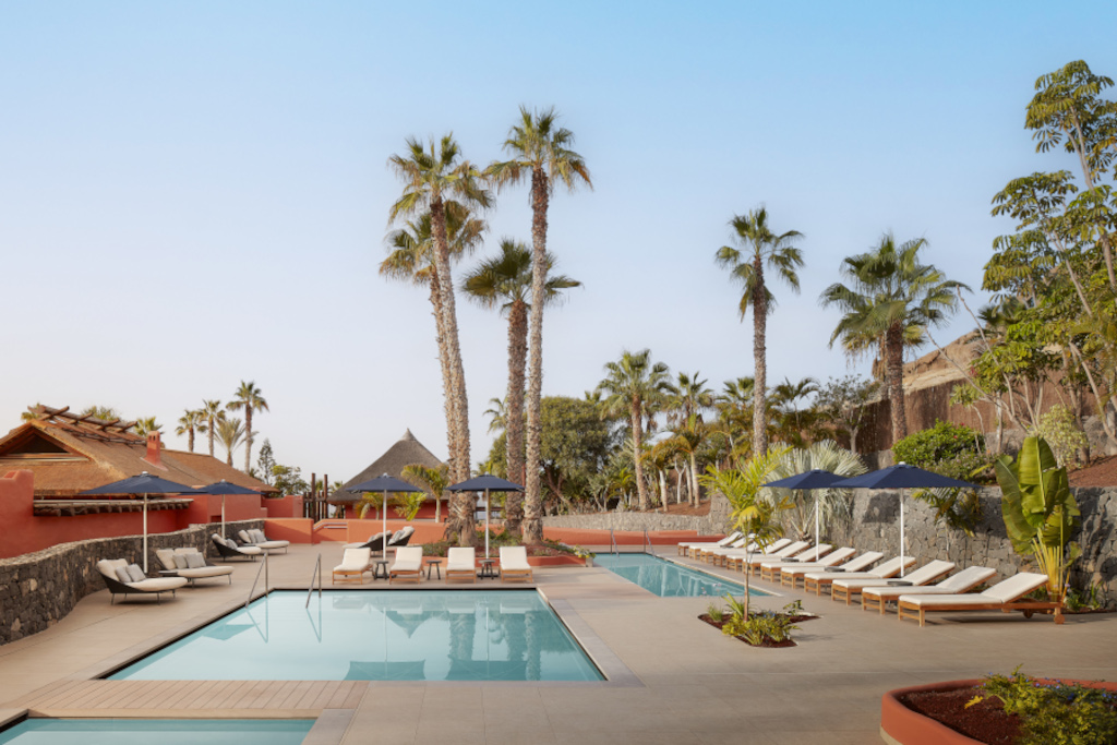 Zwembad met ligstoelen omringd door palmbomen in een complex op Tenerife.